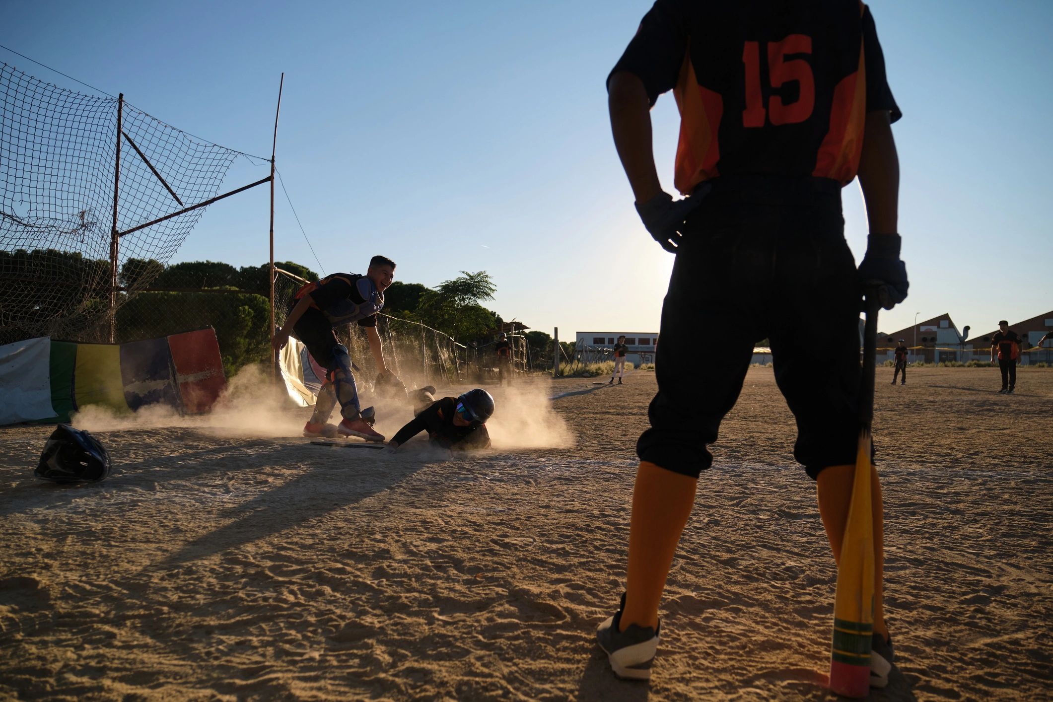 Baseball players sliding into base during game at sunset